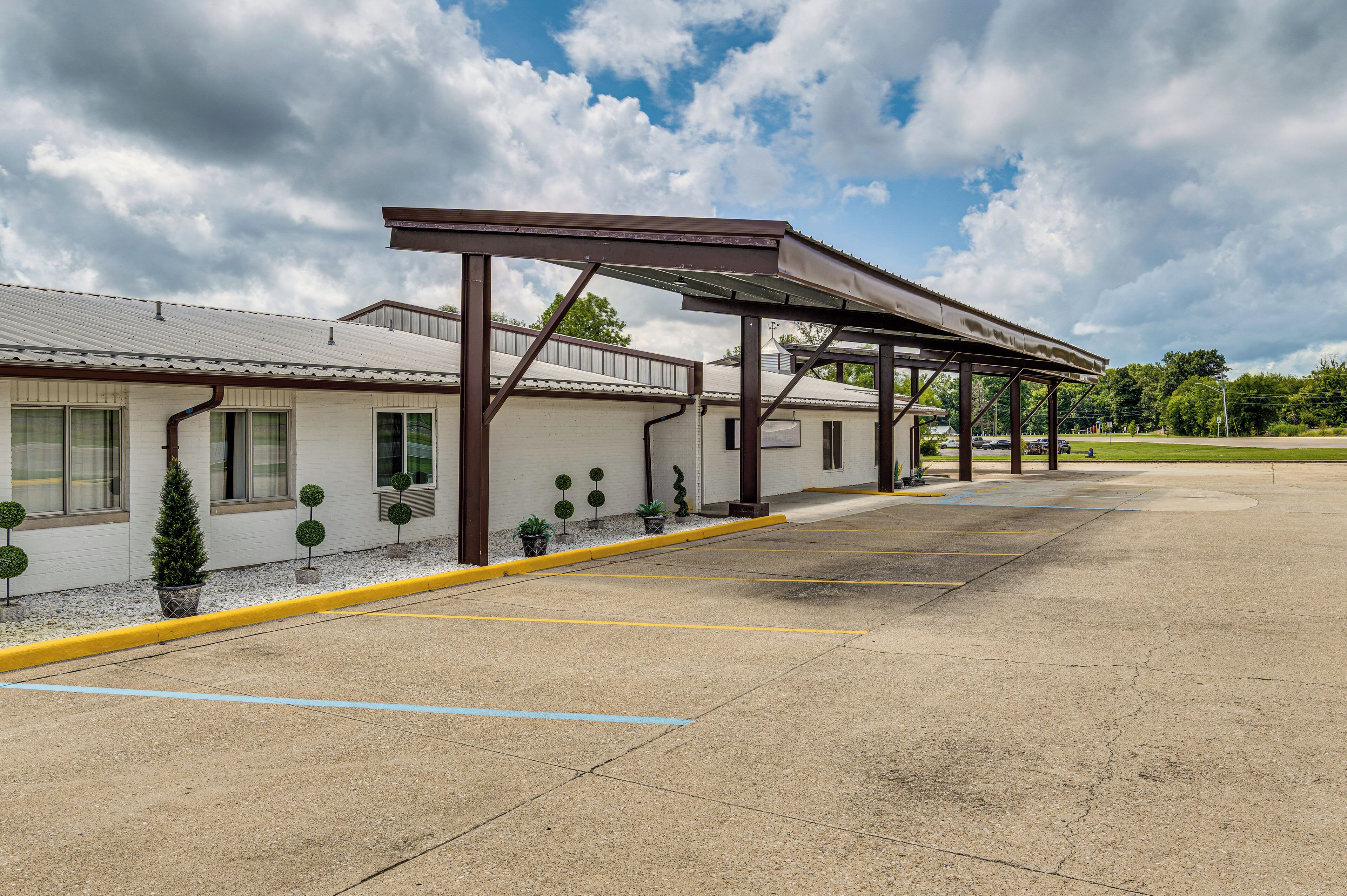 A parking lot with a building that has a covered walkway and potted plants.