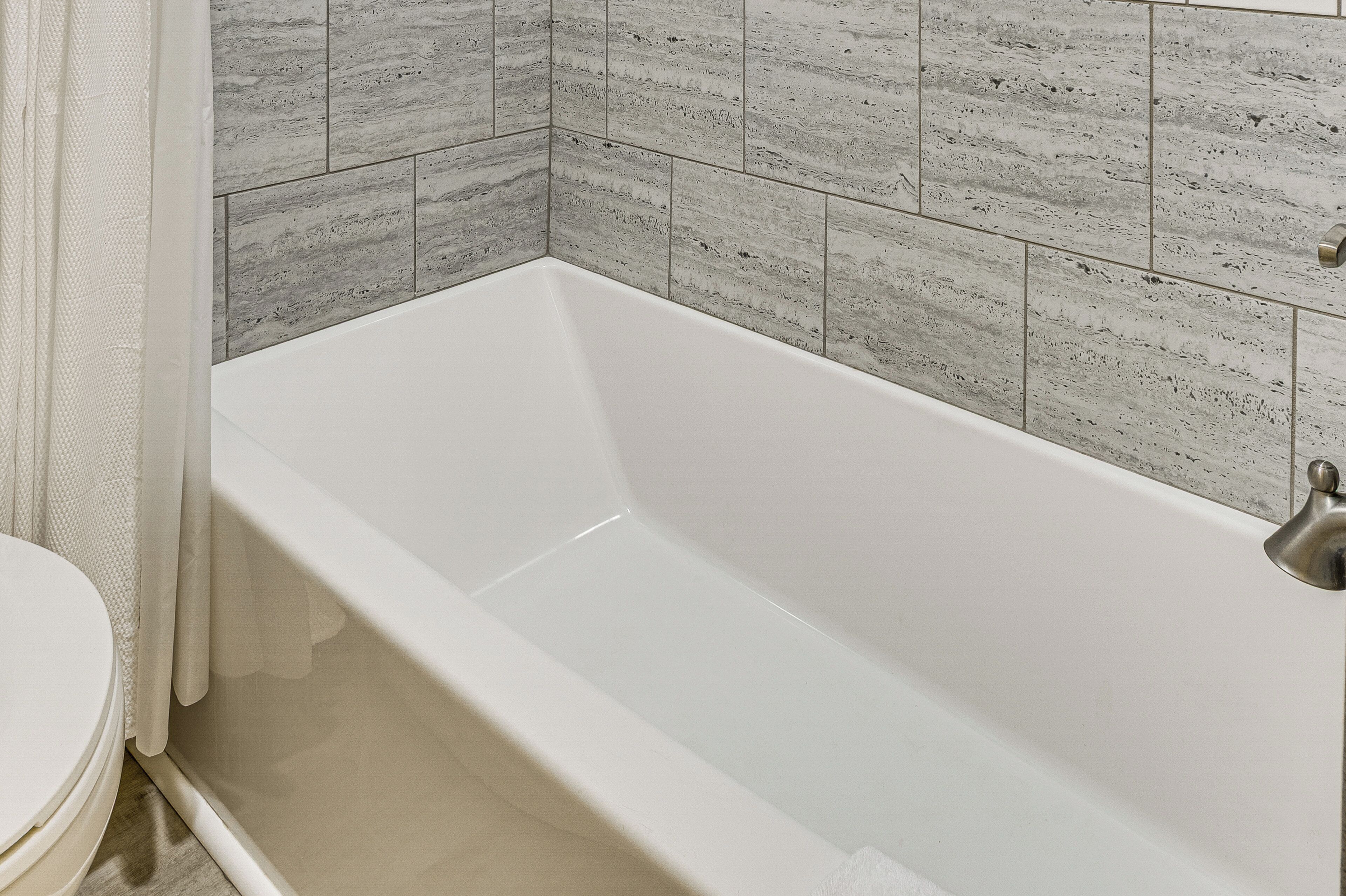 A bathtub with a white interior, adjacent to a wall with grey textured tiles.