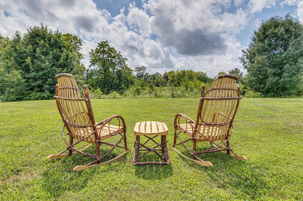 Two rocking chairs and a small table in a grassy field with trees in the background.
