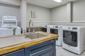 A laundry facility with a sink, multiple washing machines, and a wooden counter.