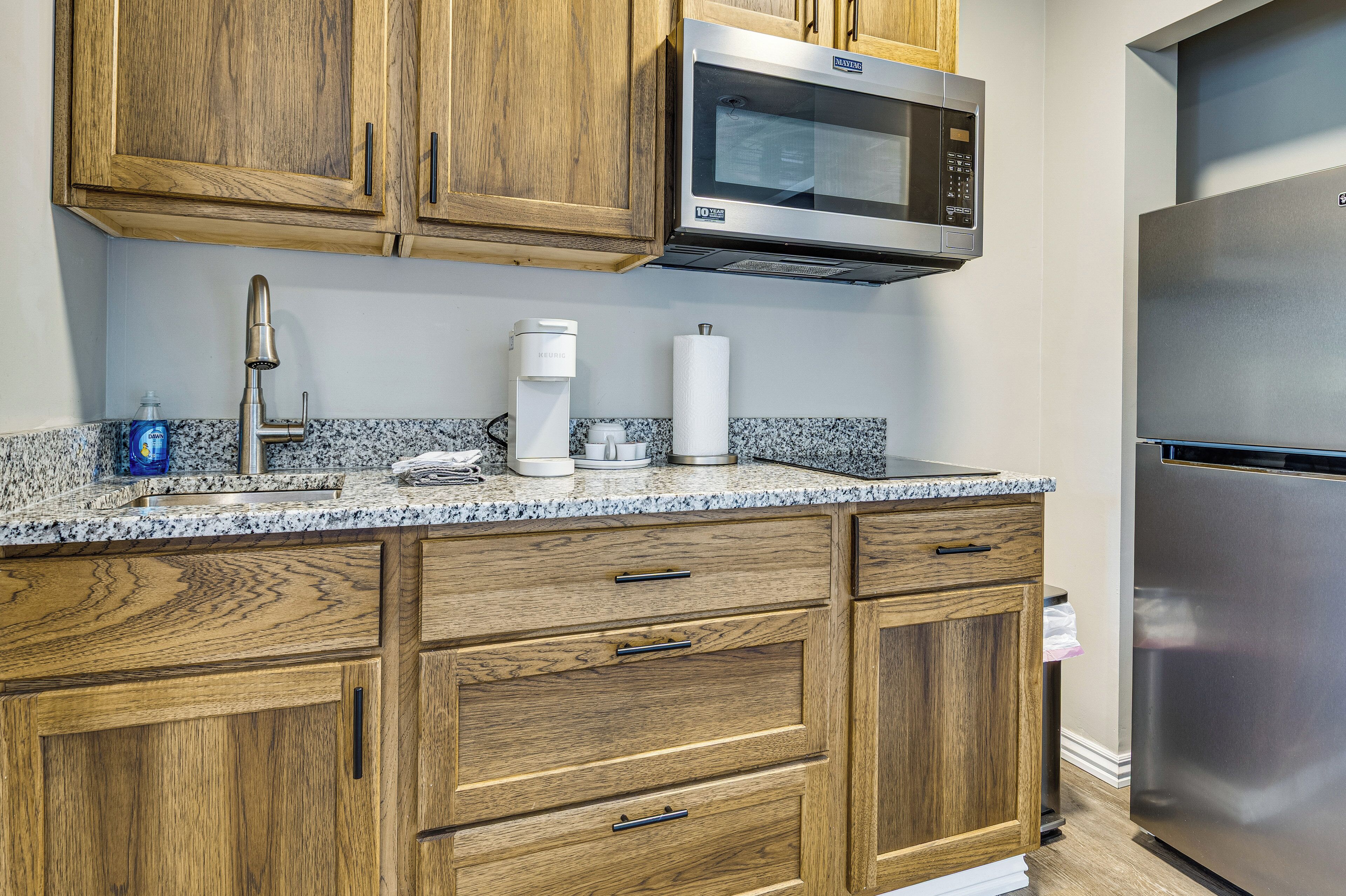 A kitchen with wooden cabinets, a built-in microwave, a coffee maker, and a stainless steel refrigerator.