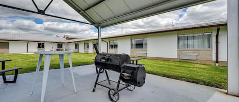 An outdoor patio with a grill, a table, and a bench.