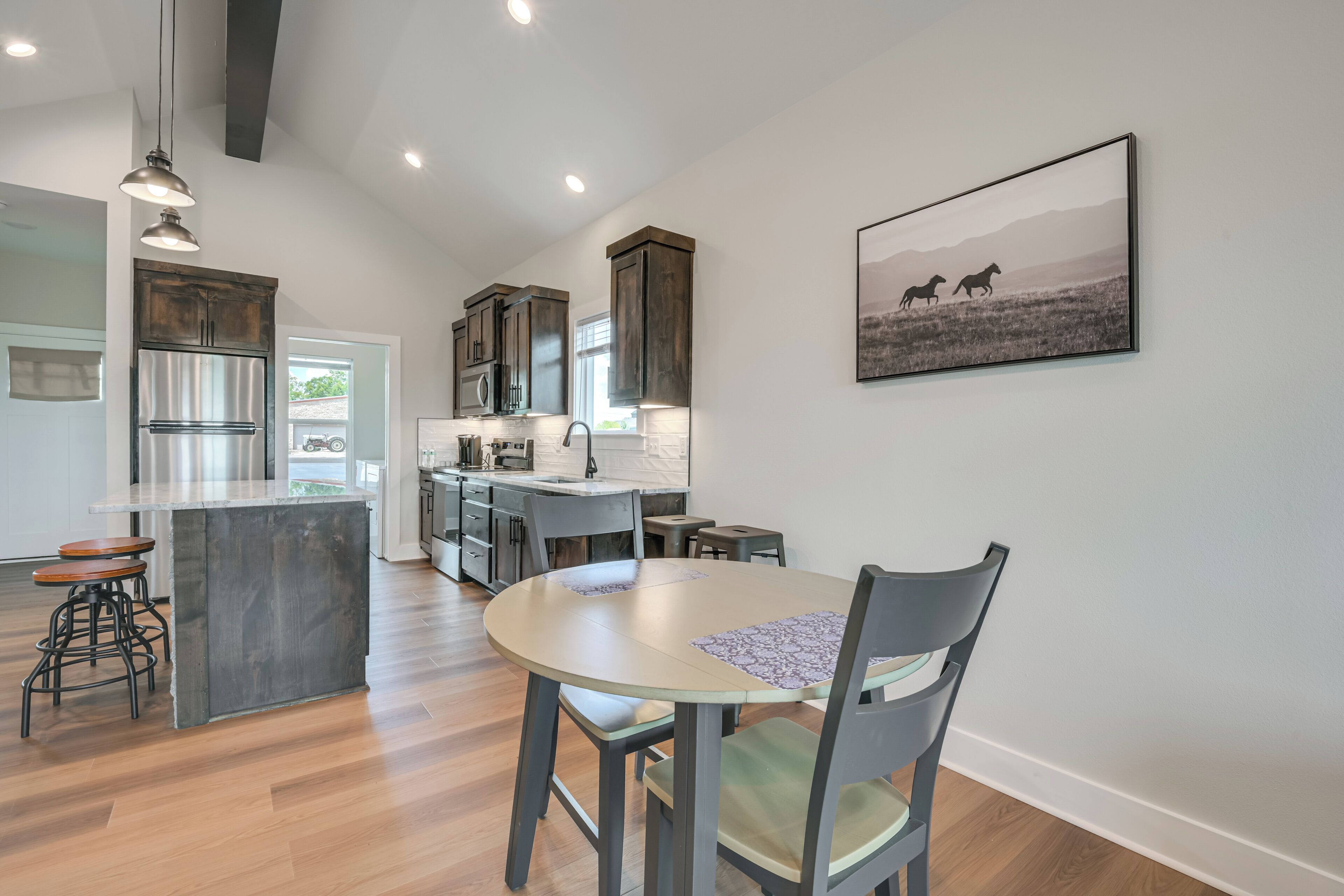 A modern kitchen with a central island, bar stools, and a dining table with chairs.