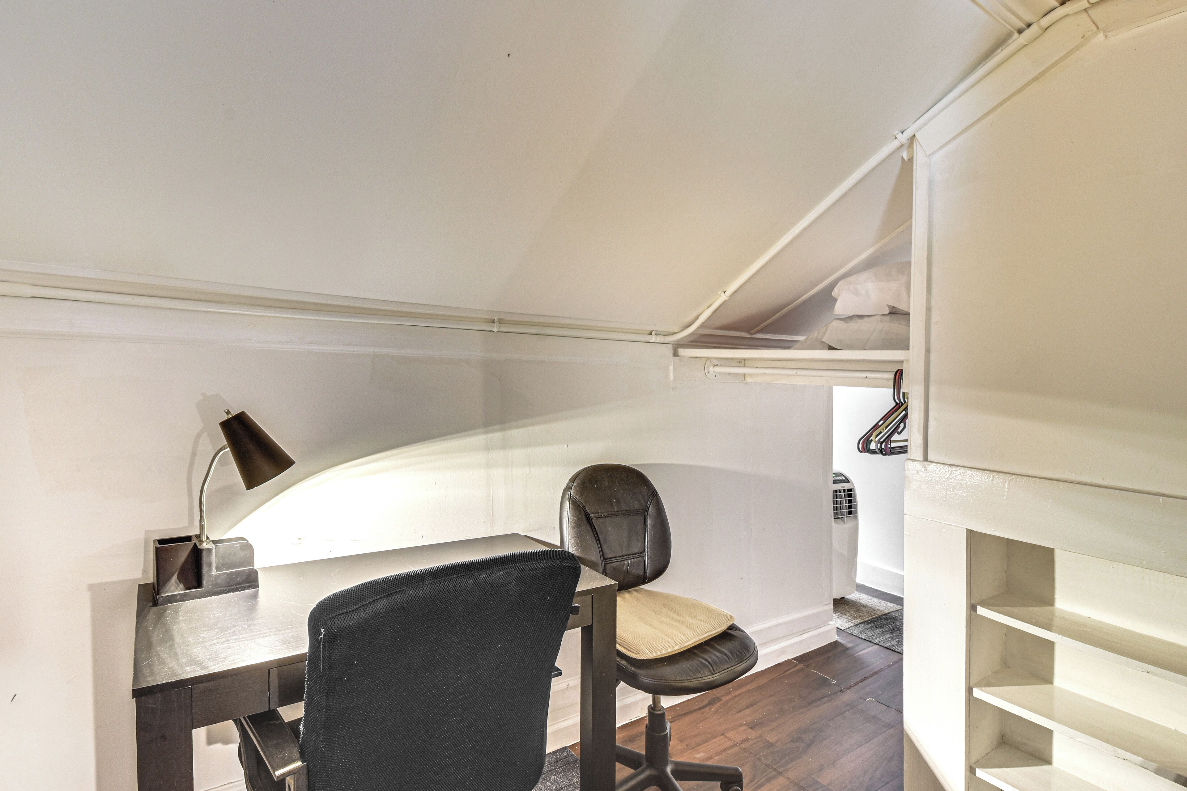 Un petit espace de bureau comprenant un bureau, une chaise, une lampe et une petite étagère.