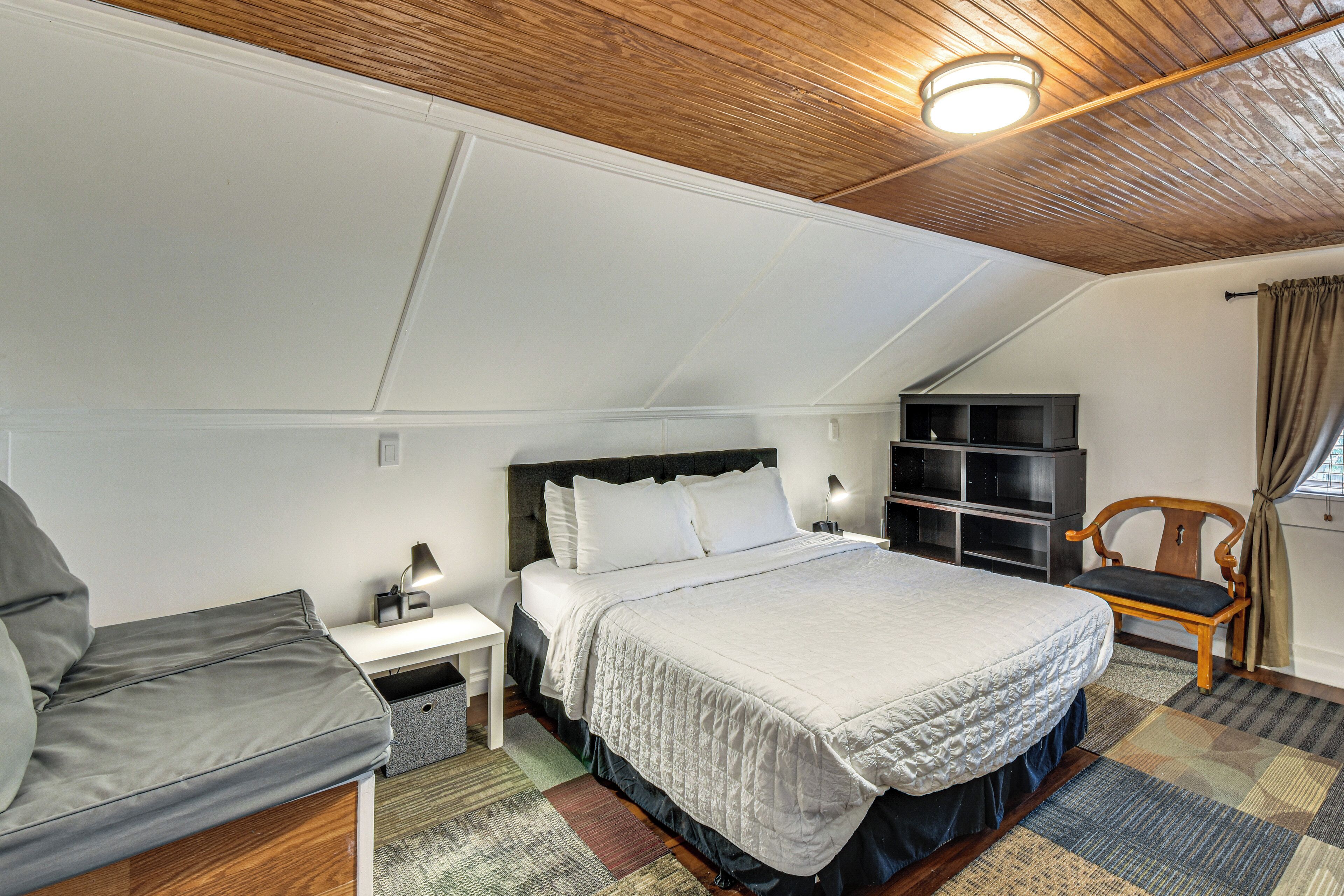 A bedroom with a bed, a nightstand, a chair, a bookshelf, and a window with curtains.