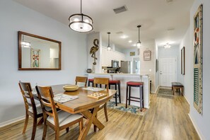 Comedor con una mesa y sillas de madera, cocina al fondo y pasillo que conduce a una puerta.