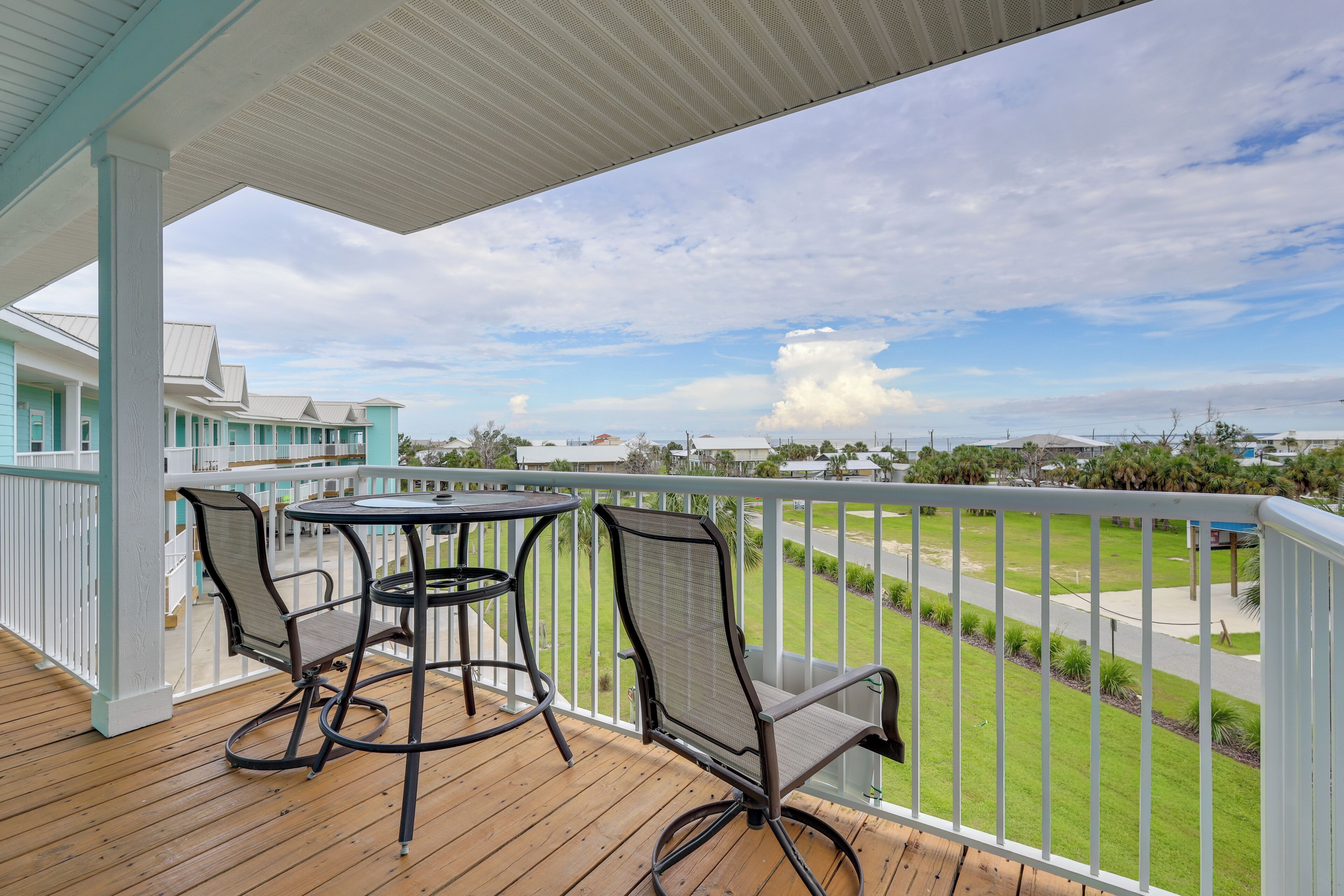 A wooden deck with a table and chairs, overlooking a grassy area with a view of distant buildings.