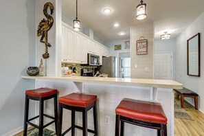 Una cocina con armarios blancos, microondas, refrigerador y una isla grande con taburetes.