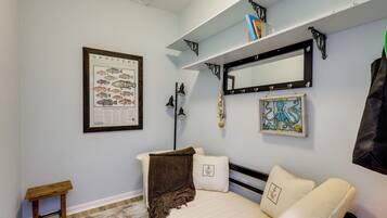 A bedroom with a bed, a small bedside table, a framed fish chart, a mirror, and a shelf with books and decorative items.