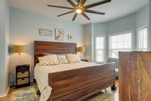 Un dormitorio con una cama de madera, dos lámparas de noche, un ventilador de techo y vistas al exterior a través de ventanas.