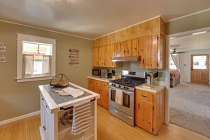 A kitchen with wooden cabinets, a gas stove, a microwave, and a small island with a cutting board and utensils.