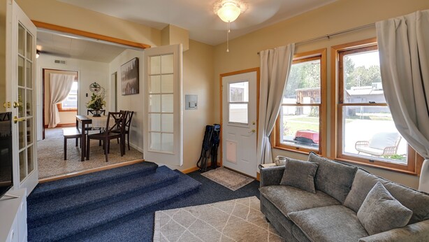 A living room with a sofa, a dining area with a table and chairs, and a staircase leading to another room.