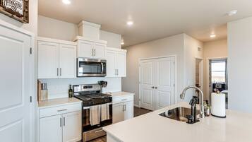 A modern kitchen with white cabinetry, a stainless steel stove, and a microwave.