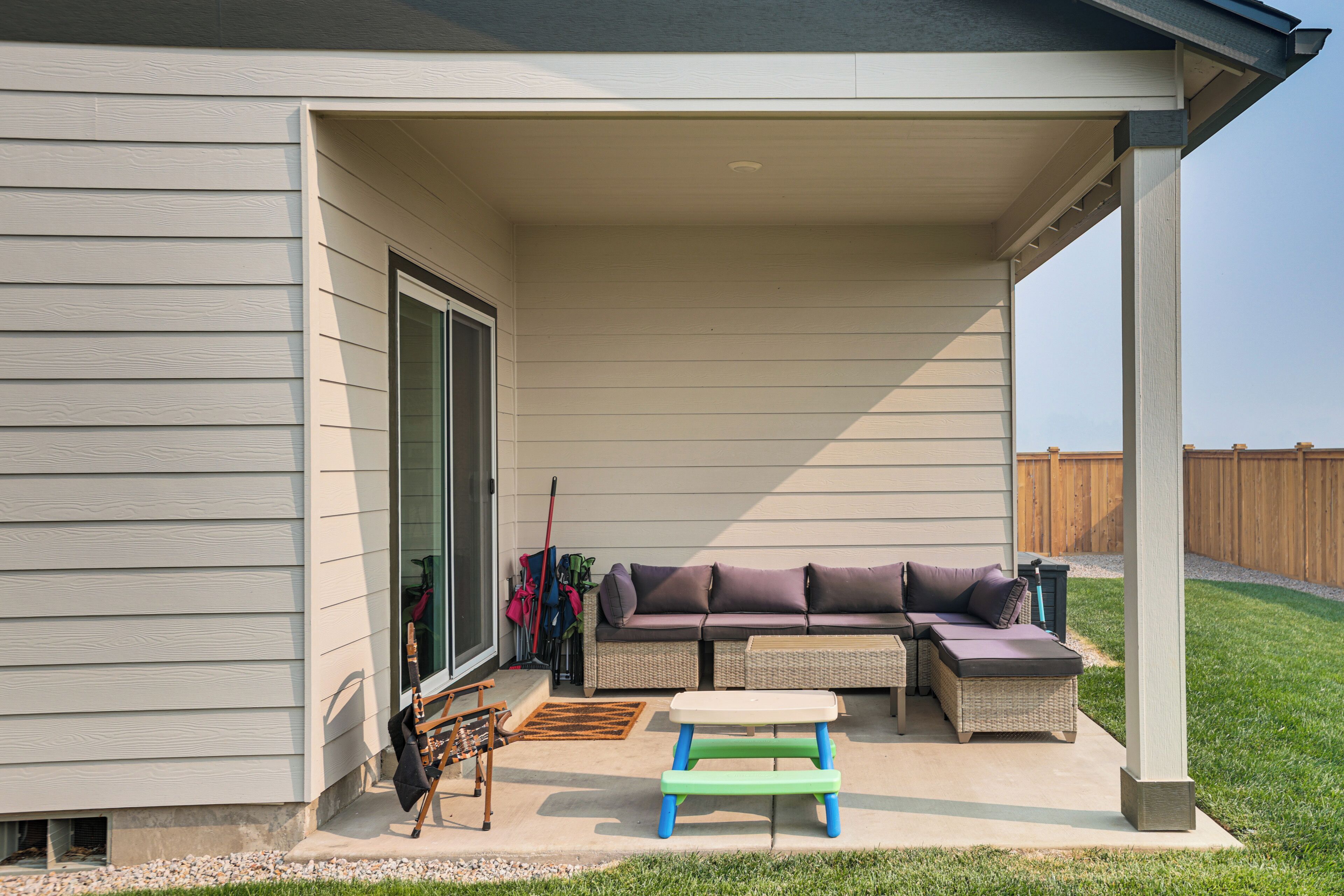 A covered patio with a sectional sofa, a small table, and outdoor furniture.