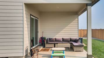 A covered patio with a sectional sofa, a small table, and outdoor furniture.