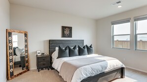 Um quarto com uma cama grande, mesa de cabeceira, cômoda, espelho e uma janela.