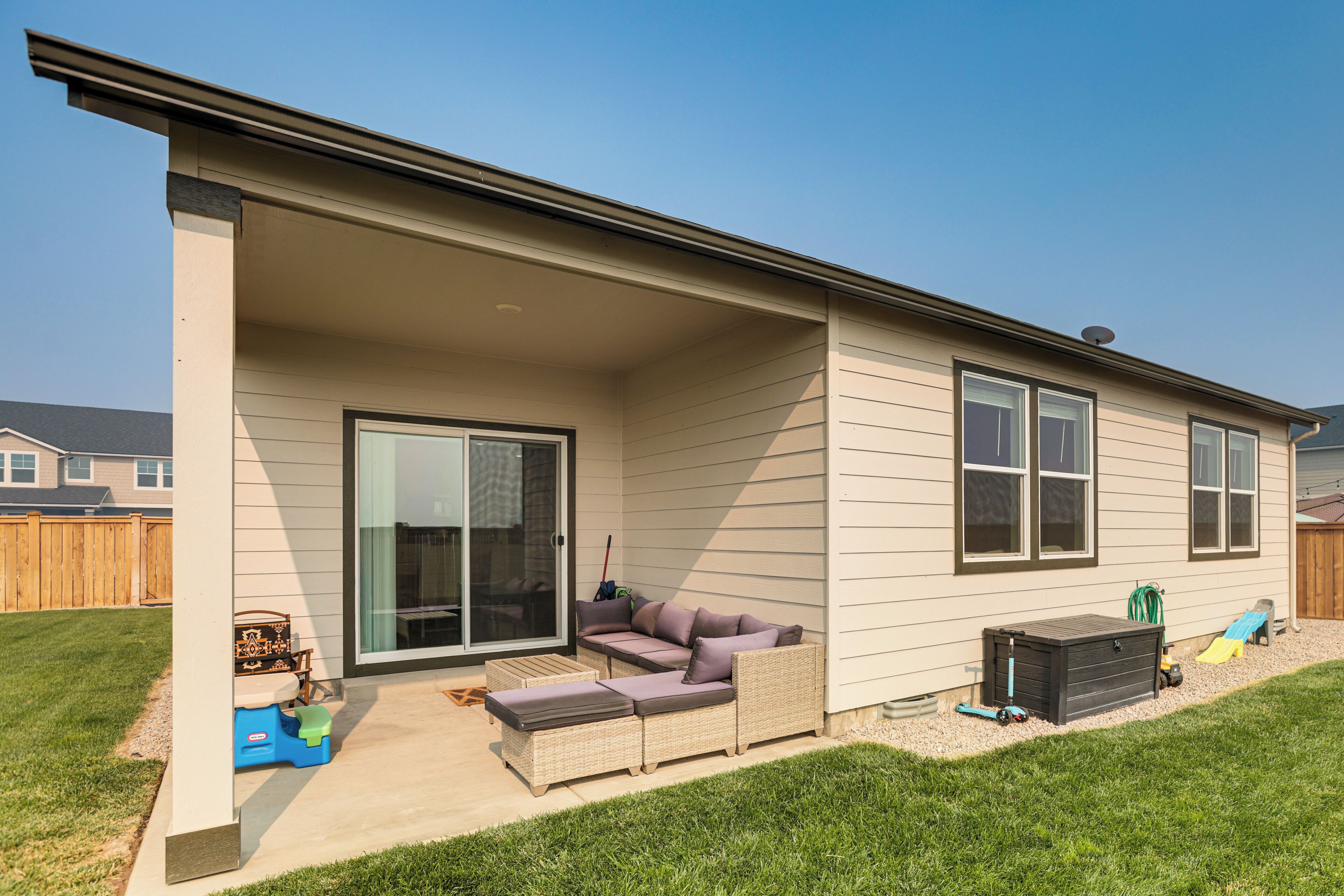 A covered patio area with a sliding glass door, a cushioned outdoor seating area, and a play structure in the background.