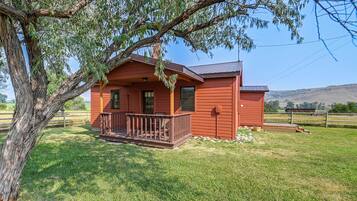 A small, single-story wooden cabin with a porch and a fenced yard.