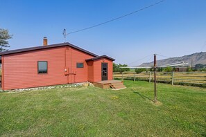 A red building with a small porch and a chimney, surrounded by a grassy area and a wooden fence. - Stillwater River Cabin: Private Access to Fishing (Absarokee)