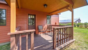 A wooden porch with a railing, a bench, and a chair.