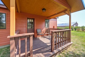 A wooden porch with a railing, a bench, and a chair.