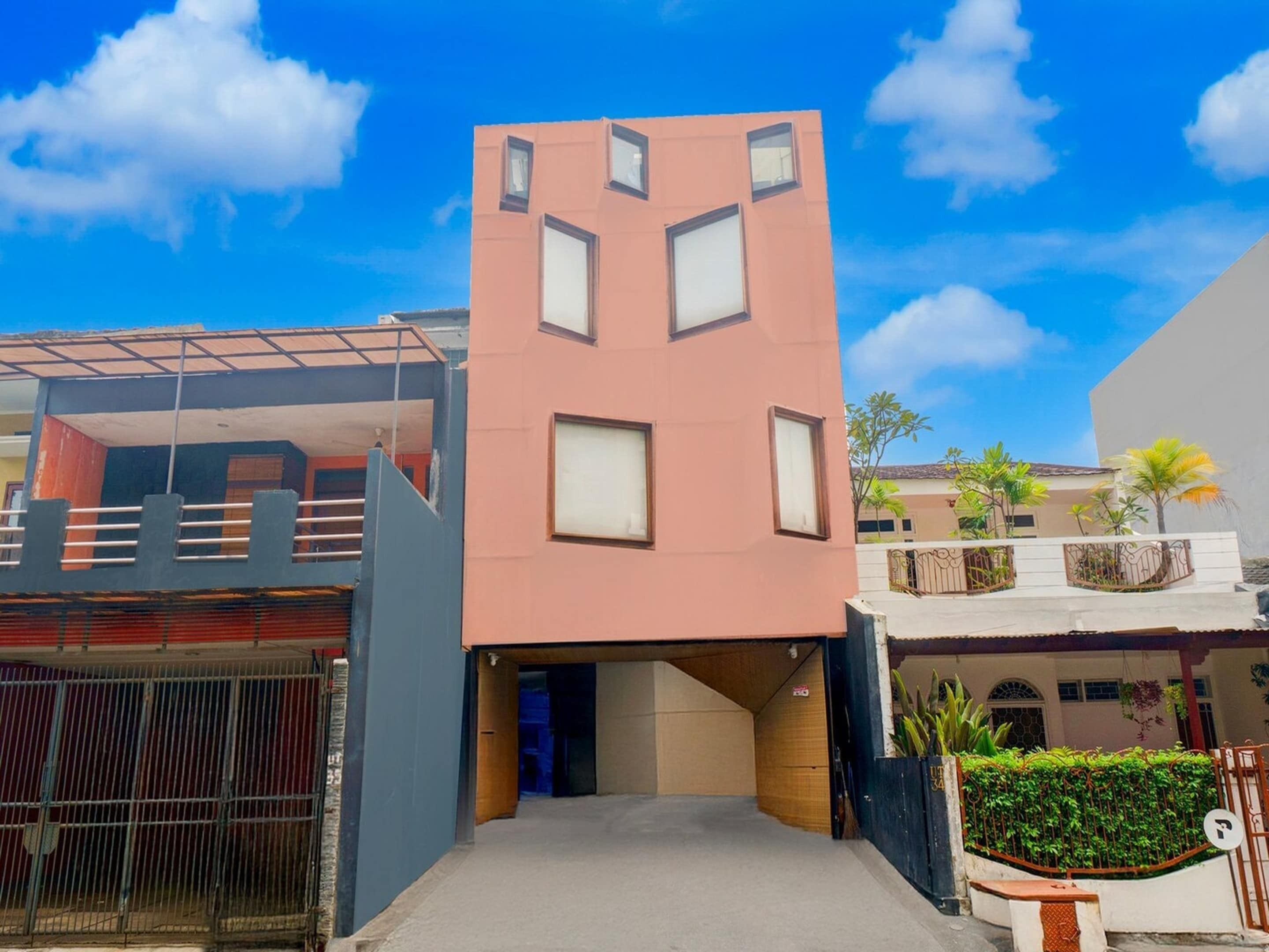 Un edificio moderno con fachada geométrica distintiva, un acceso cubierto y una zona ajardinada delimitada por una reja.