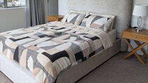 A modern bedroom with a large bed, a bedside table, and a window with curtains.