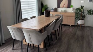 A modern dining area with a wooden table, grey upholstered chairs, a wooden cabinet, and a potted plant.