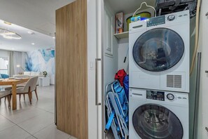 A compact living space with a dining area, a washing machine, and a stroller. - HH-2Bdr415 - Aruba's Amazing 2BDR Retreat. (Oranjestad)