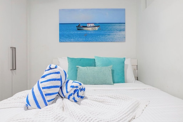 A hotel room with a bed, a painting of a boat on the wall, and a view of the sea.
