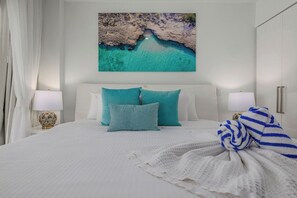 A bedroom with a bed, pillows, a blanket, and a painting of a beach scene.