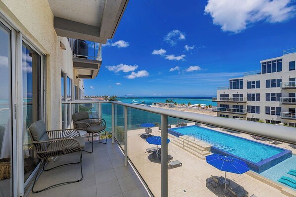 A balcony with a view of a swimming pool and the ocean.