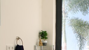 Um banheiro com pia branca, porta-toalhas, prateleira de vidro com toalhas, planta em vaso e janela com vista para árvores.