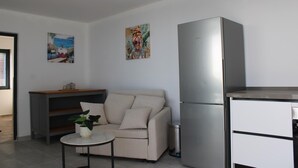 Um espaço de estar compacto com cozinha compacta, um sofá, uma pequena mesa com uma planta e obras de arte nas paredes.