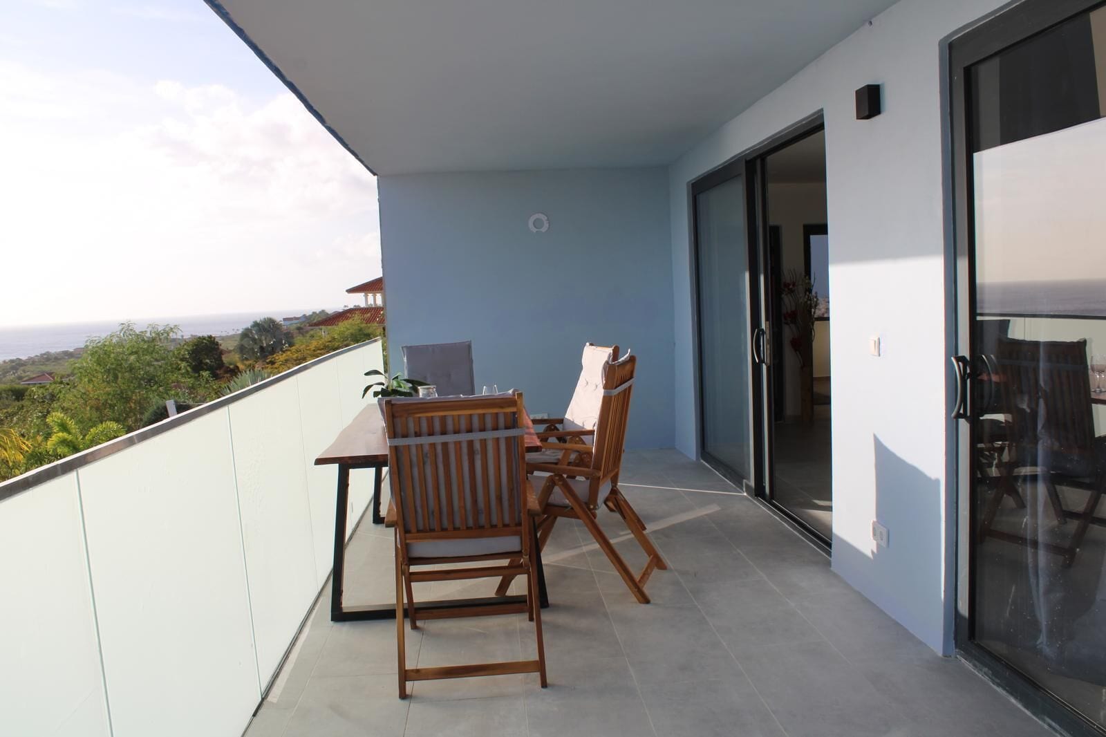A balcony with a table and chairs, a sliding glass door, and a view of the landscape.