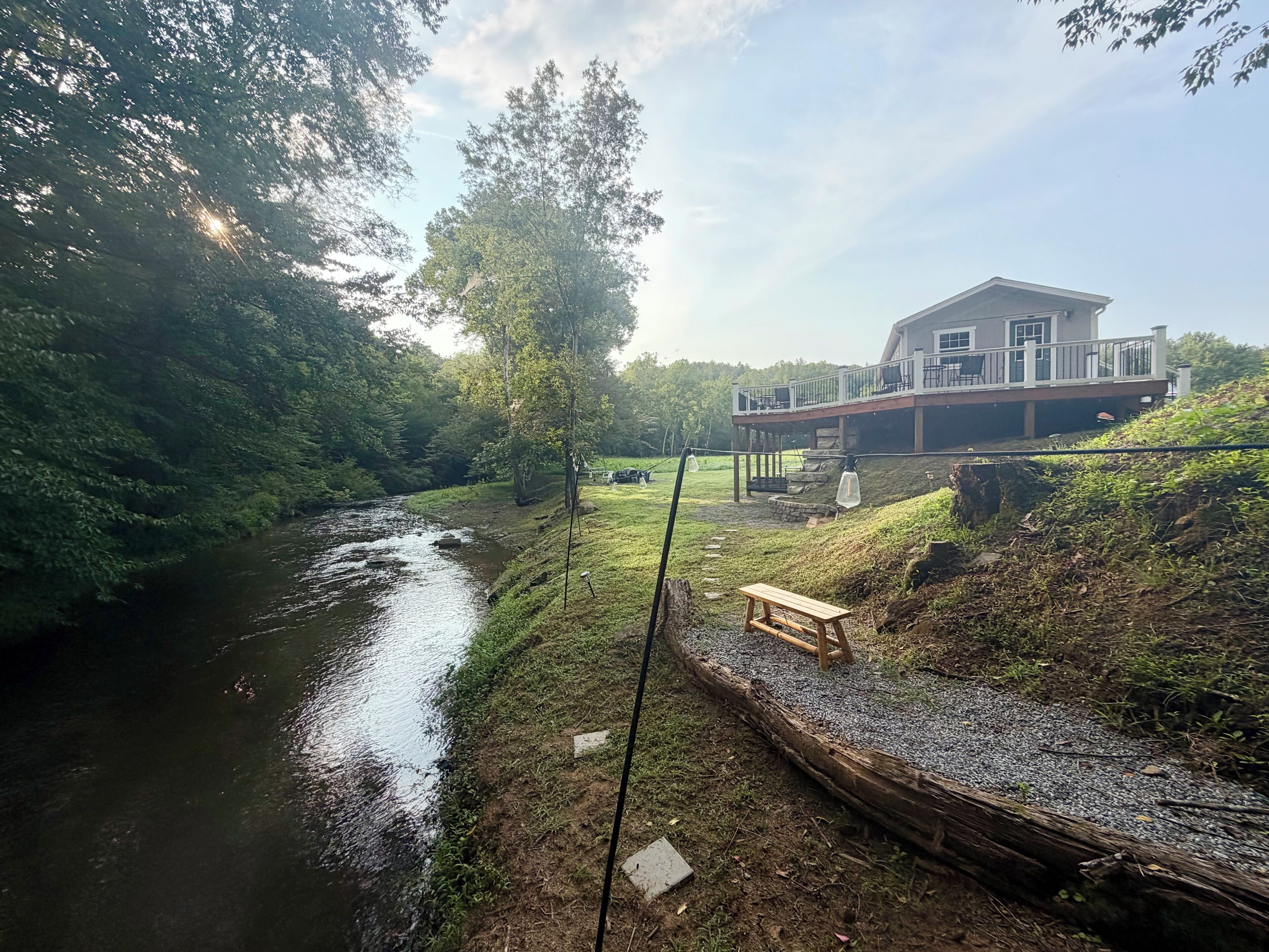 Une propriété située au bord de la rivière, dotée d’une terrasse en bois, d’un banc et d’une maison avec un balcon.