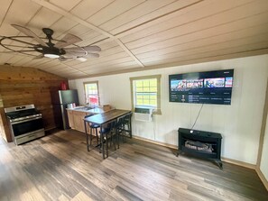 Eine Küche mit Holzboden, einem Herd, einem Kühlschrank, einem Esstisch mit Stühlen und einem an der Wand montierten Fernseher, der ein Programm zeigt.