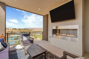 A balcony with a pool view, a flat-screen TV, and a fireplace. - Courtside Sunsets: Near Pickleball Courts and Pool (St. George)