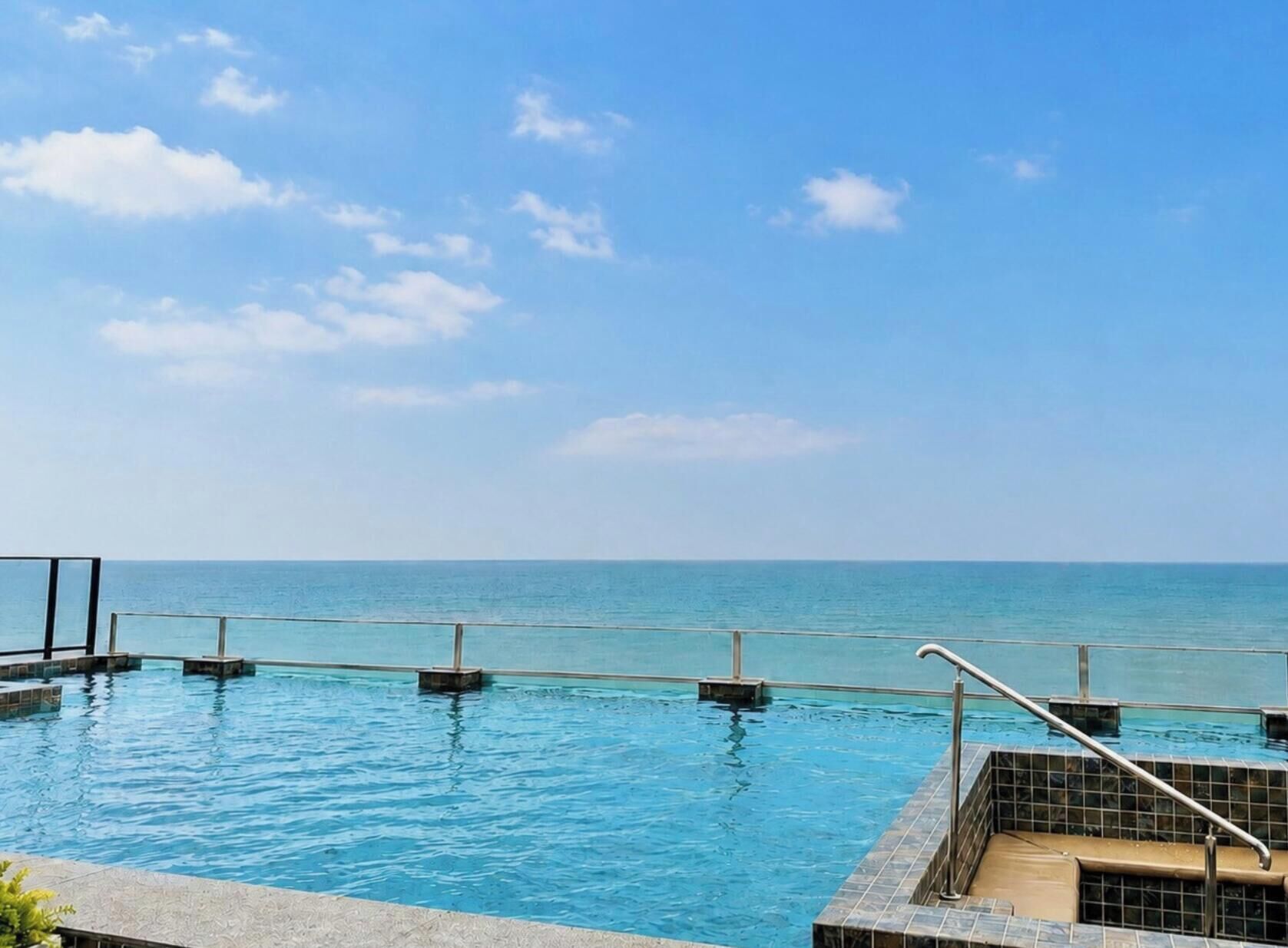 A swimming pool with a view of the sea, surrounded by a tiled deck and a metal railing.