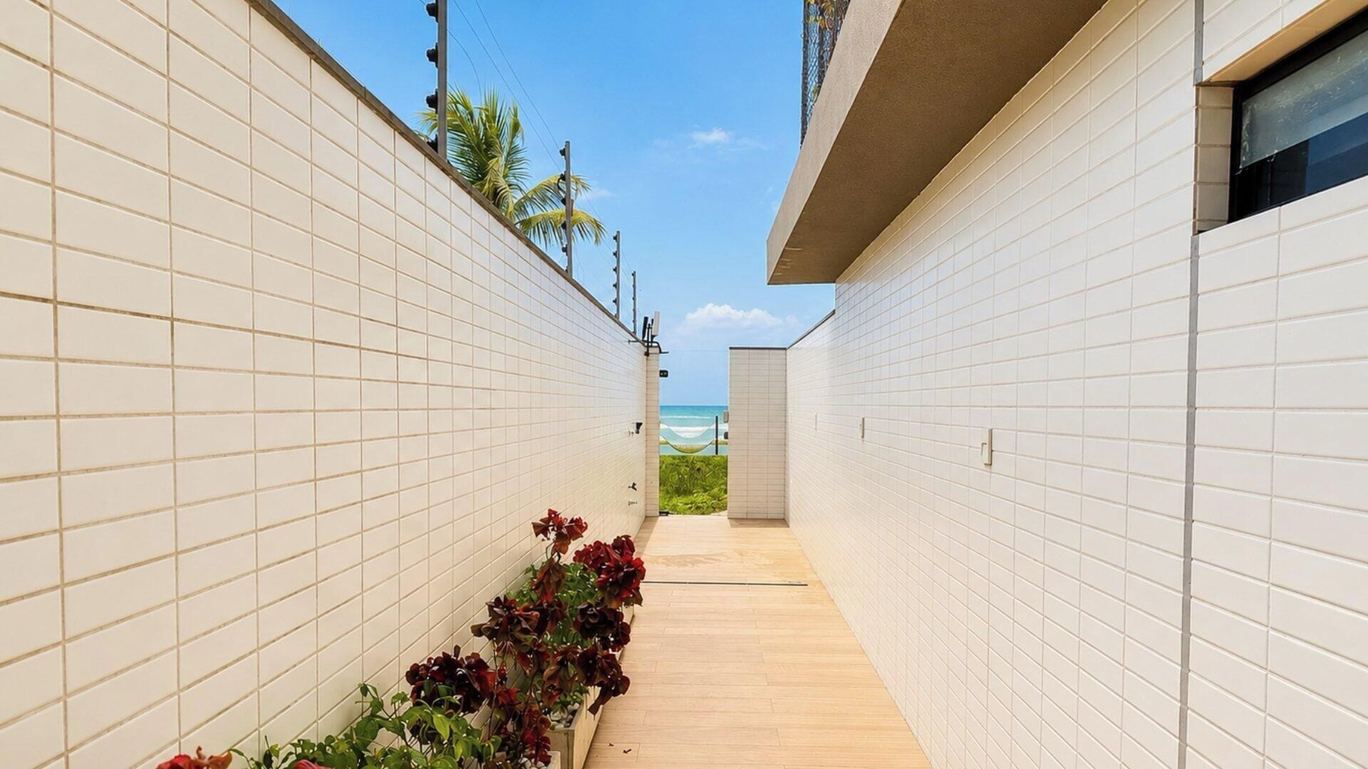 A narrow corridor with white tiled walls, a wooden floor, and a view of the ocean.