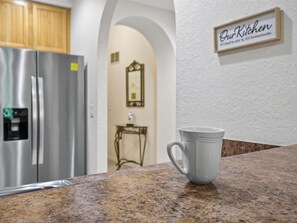 Eine Küche mit einem Edelstahl-Kühlschrank, einer weißen Tasse auf der Arbeitsfläche und einem Schild mit der Aufschrift 'Our Kitchen'.