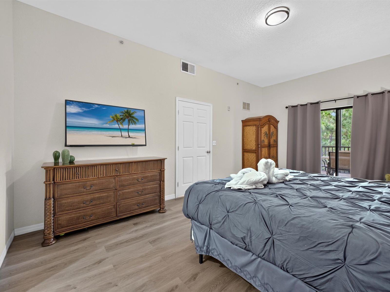 A bedroom with a bed, a dresser, a painting, a wardrobe, and a view through a door.