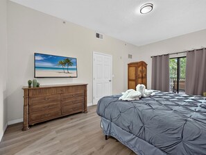Ein Schlafzimmer mit Bett, Schminktisch, einem Bild, einem Kleiderschrank und Blick durch eine Tür.
