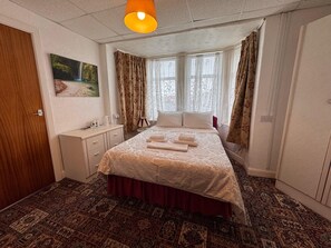 Ein Hotelzimmer mit einem Bett, einem Nachttisch, einem Gemälde und einem Fenster mit Vorhängen.