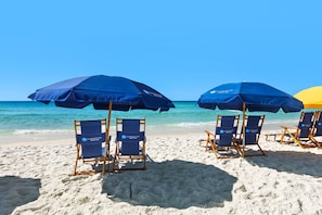 Strandliegen und Sonnenschirme an einem sandigen Strand, im Hintergrund das Meer.