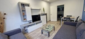 Ein modernes Wohnzimmer mit Fernseher, Glastisch und grauen Sofas.