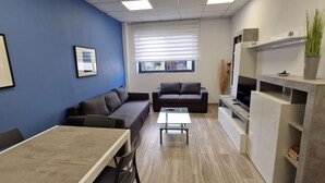 A modern office space with a dining area, sofas, a TV, and a plant. - Enjoy a comfortable stay in this modern 1-bedroom apartment in Sliema, Malta. Featuring a spacious living area, private bedroom, equipped kitchen and bathroom, it is an ideal base for couples, solo travellers or business stays. (Tas-Sliema)