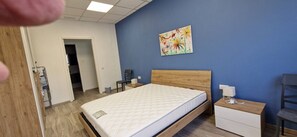 A bedroom with a bed, bedside tables, a chair, a painting, and a door leading to another room. - Enjoy a comfortable stay in this modern 1-bedroom apartment in Sliema, Malta. Featuring a spacious living area, private bedroom, equipped kitchen and bathroom, it is an ideal base for couples, solo travellers or business stays. (Tas-Sliema)