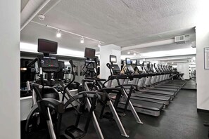 Ein Fitnessraum mit mehreren Laufbändern und Crosstrainern, die in Reihen angeordnet sind.