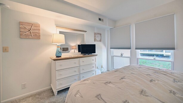 Quarto com cama, penteadeira, televisão e janela com persianas.